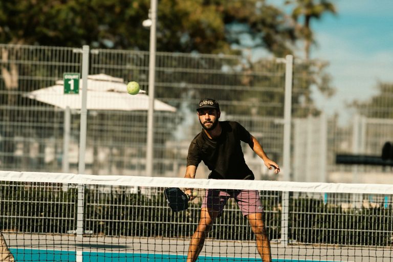 intermediate pickleball player hitting a served shot with paddle on outdoor sunny court